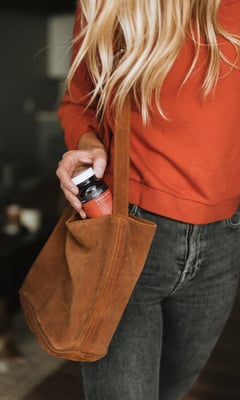 Women pulling out a supplement bottle from her leather tote bag.
