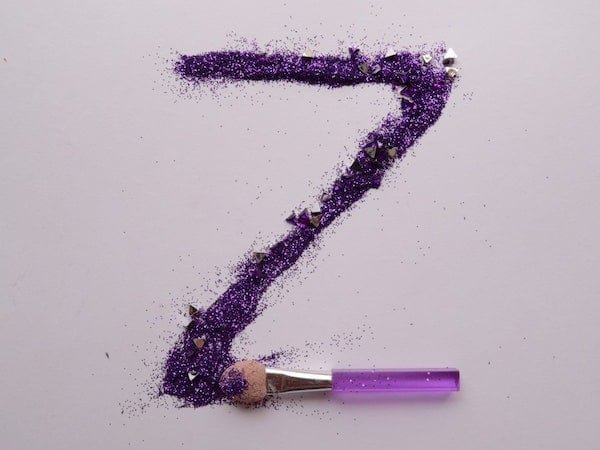 The letter Z spelled out in purple glitter with a paintbrush, by Zyanya BMO via Unsplash.