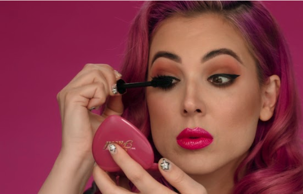 A woman applying Too Faced’s Damn Girl mascara.