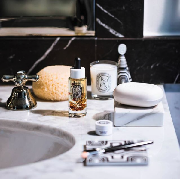 A close-up photo of a bathroom counter featuring a Diptyque Roses candle.