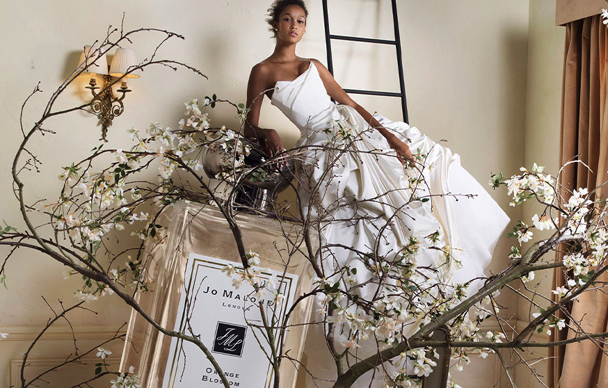 An advertisement for Jo Malone, featuring a giant bottle of Orange Blossom perfume and a woman wearing a wedding dress.