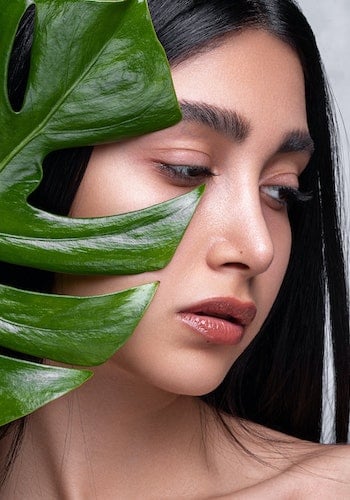 A portrait of a skincare influencer posing with a large green plant leaf, by Ahmad Ebadi. 