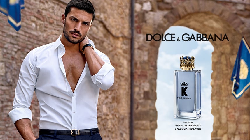 Italian influencer Mariano Di Vaio poses against a castle wall in a white shirt next to Dolce & Gabbana Beauty’s K Eau de Toilette.