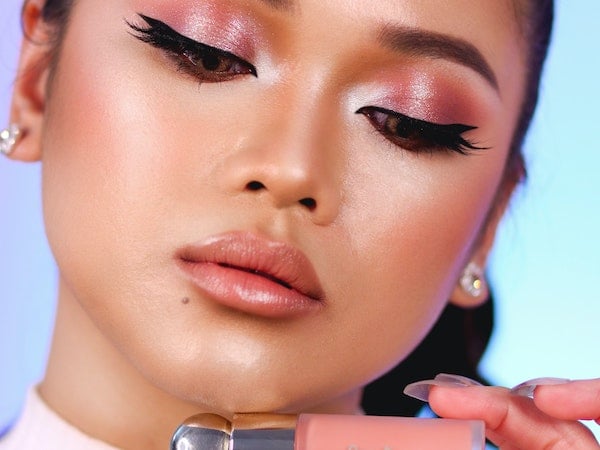 A beauty influencer holds a lip gloss from celebrity beauty brand Rare Beauty, by Vince Mariel Conlu via Unsplash.