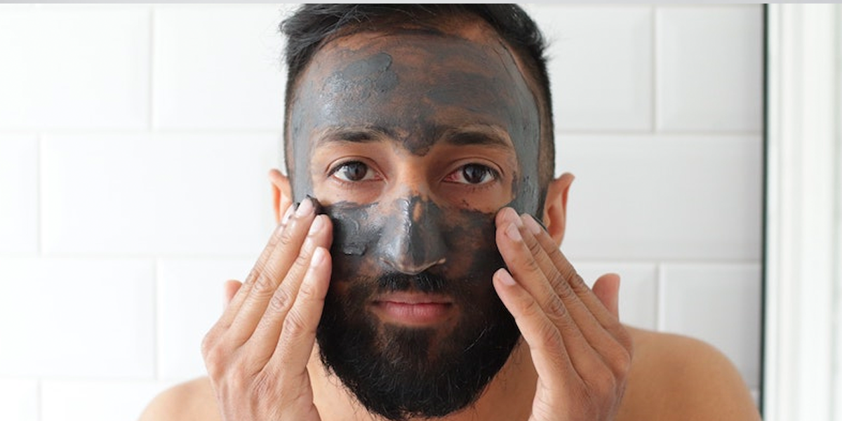 A bearded man applies a charcoal mask, by Safia Shakil.