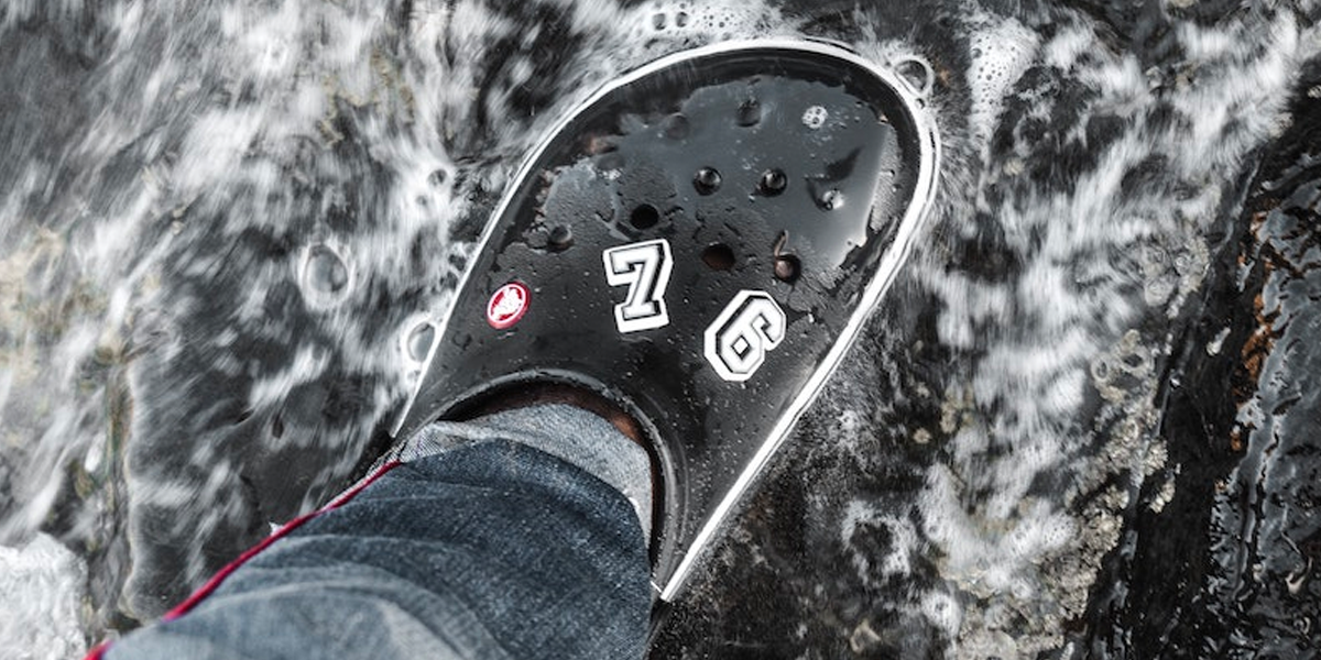 A close-up photo of a black Crocs sandal with jibbitz, by Blessing Shock. 