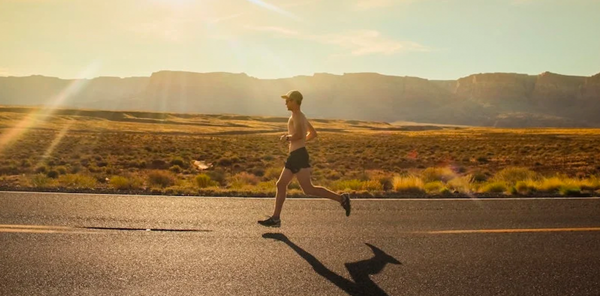 A man running on a road with mountains behind him, by Isaac Wendland.