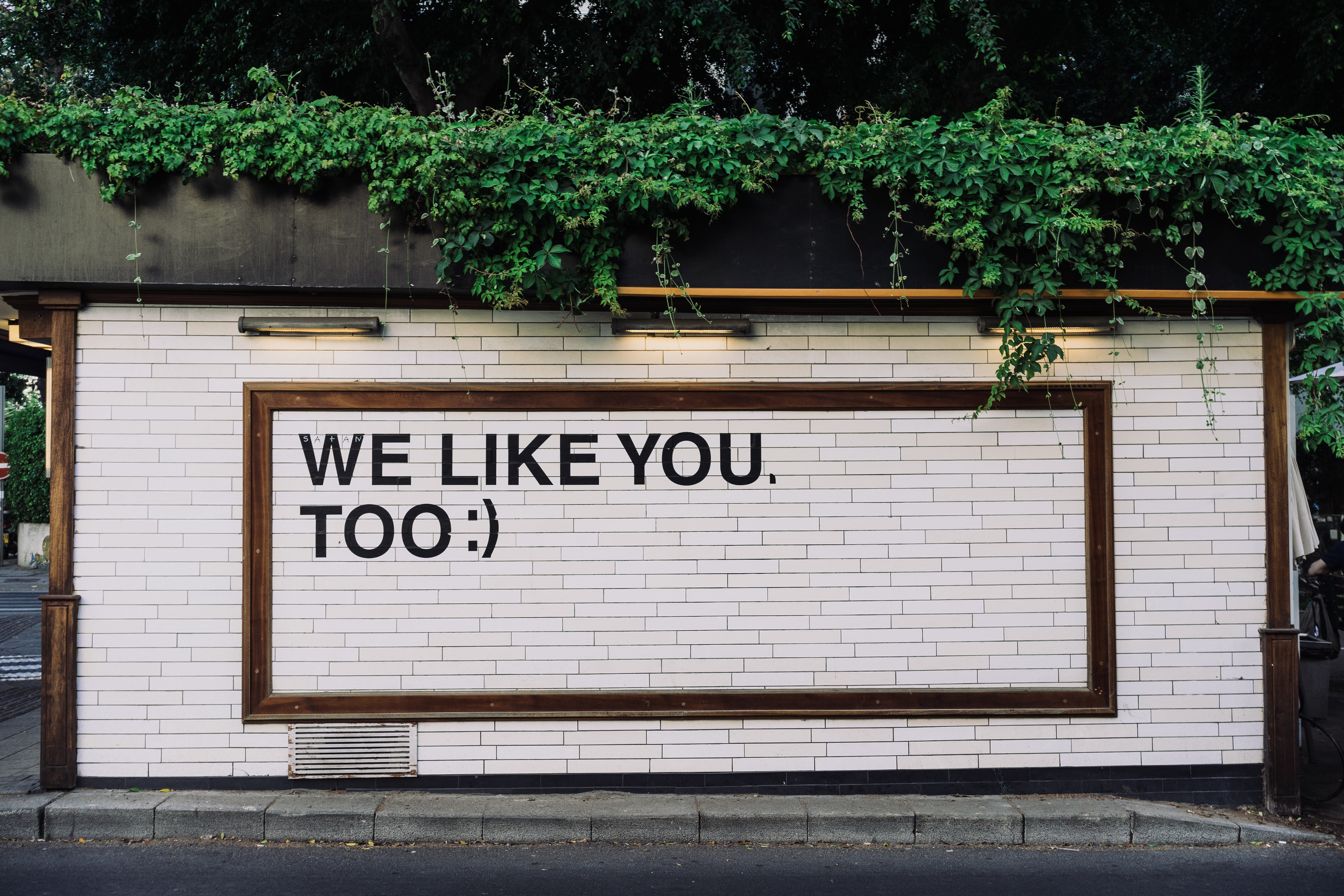 A photo of a white brick wall with the phrase “We Like You, Too :)” printed on it.