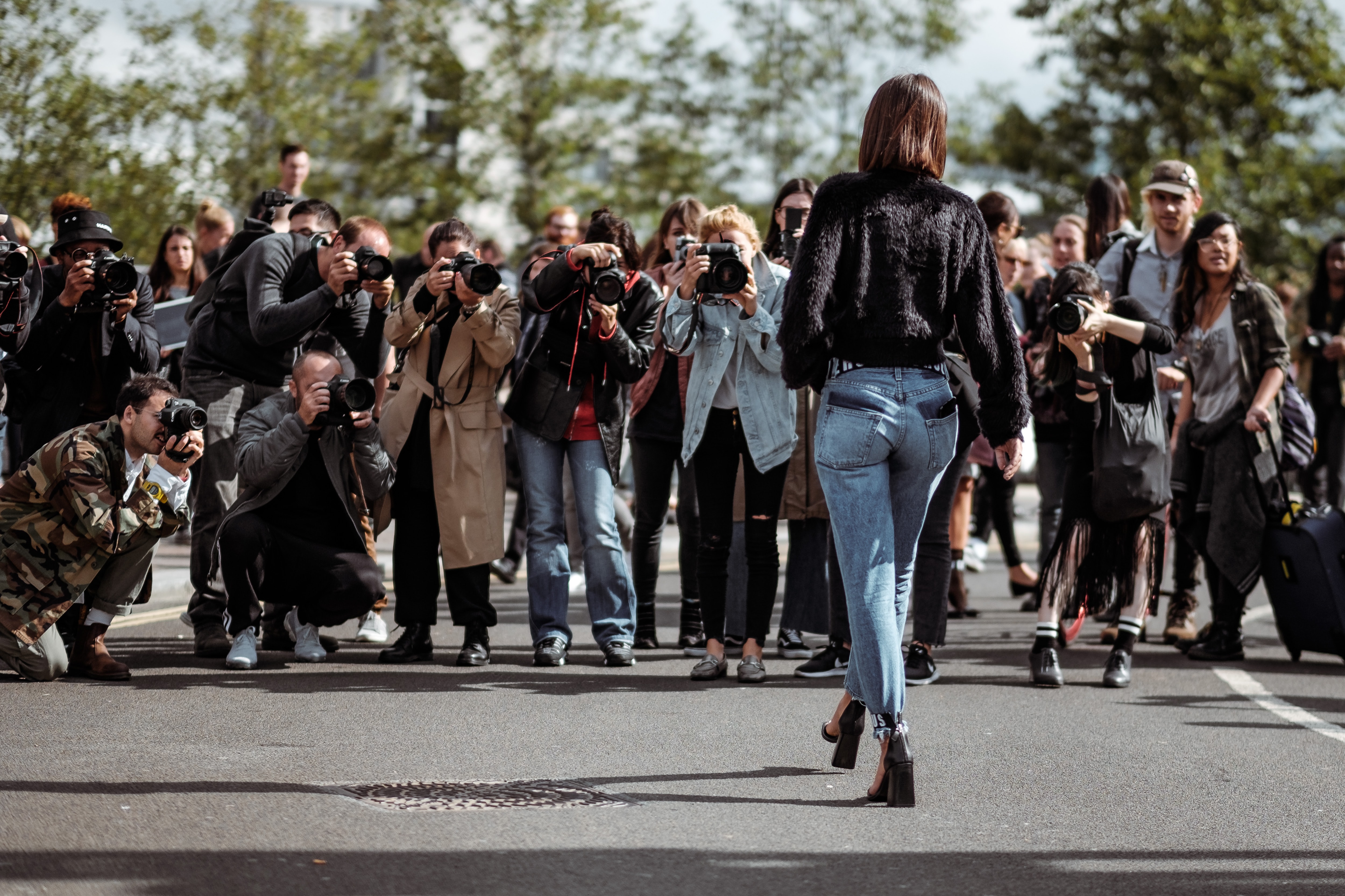 A photo of a woman from behind being photographed by a large group of photographers.