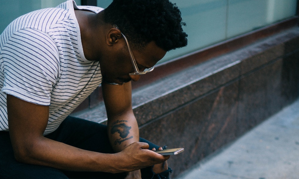 A top influencer with glasses looking at a smartphone while seated outside, by Derick Anies via Unsplash.