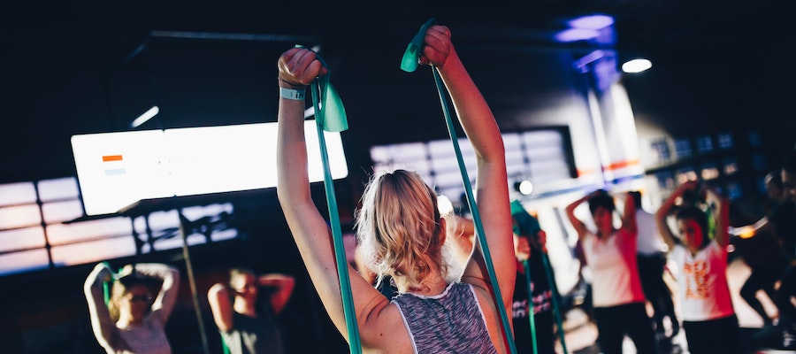 A group of women using resistance bands in a boutique fitness studio, by Geert Pieters. 