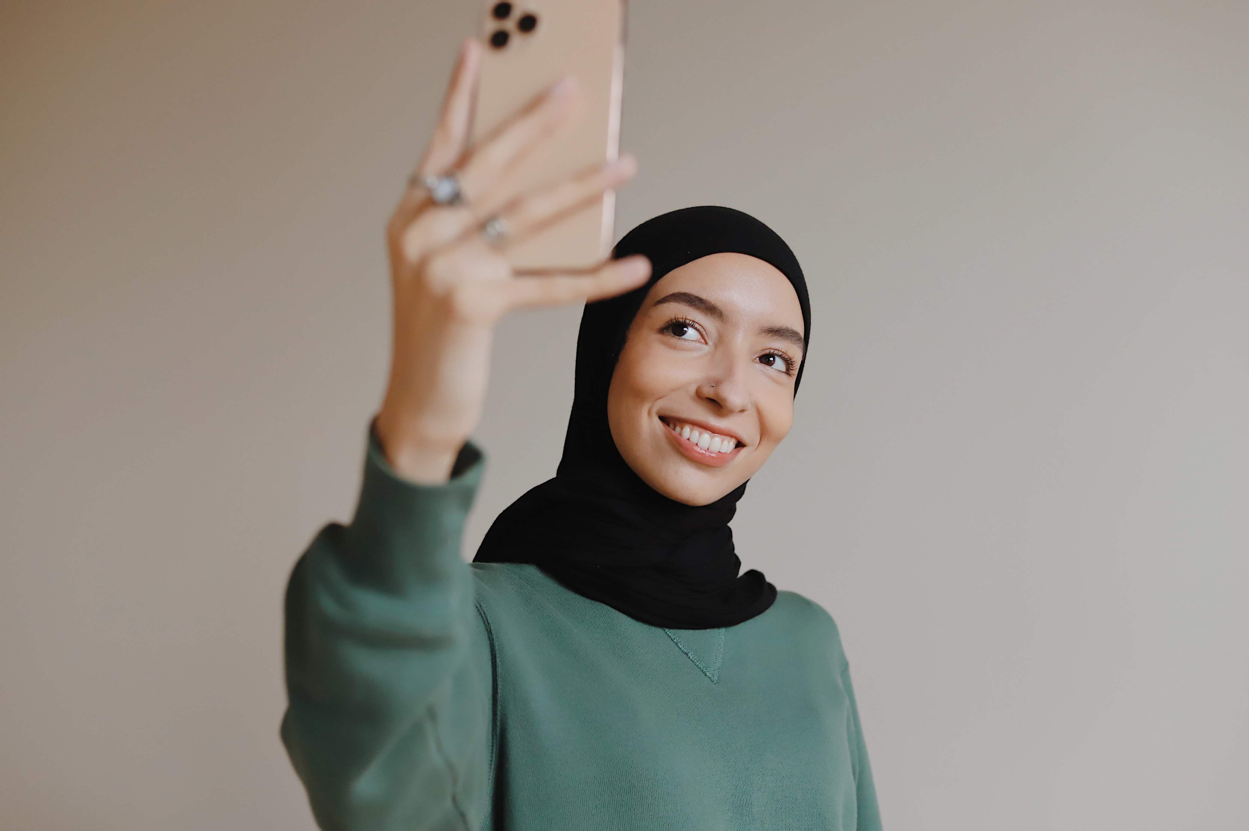 An influencer wearing a hijab takes a selfie.