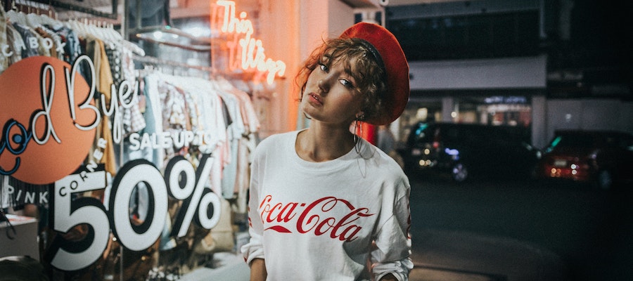 An influencer standing in front of a storefront with a sale sign, by Joshua Rawson. 