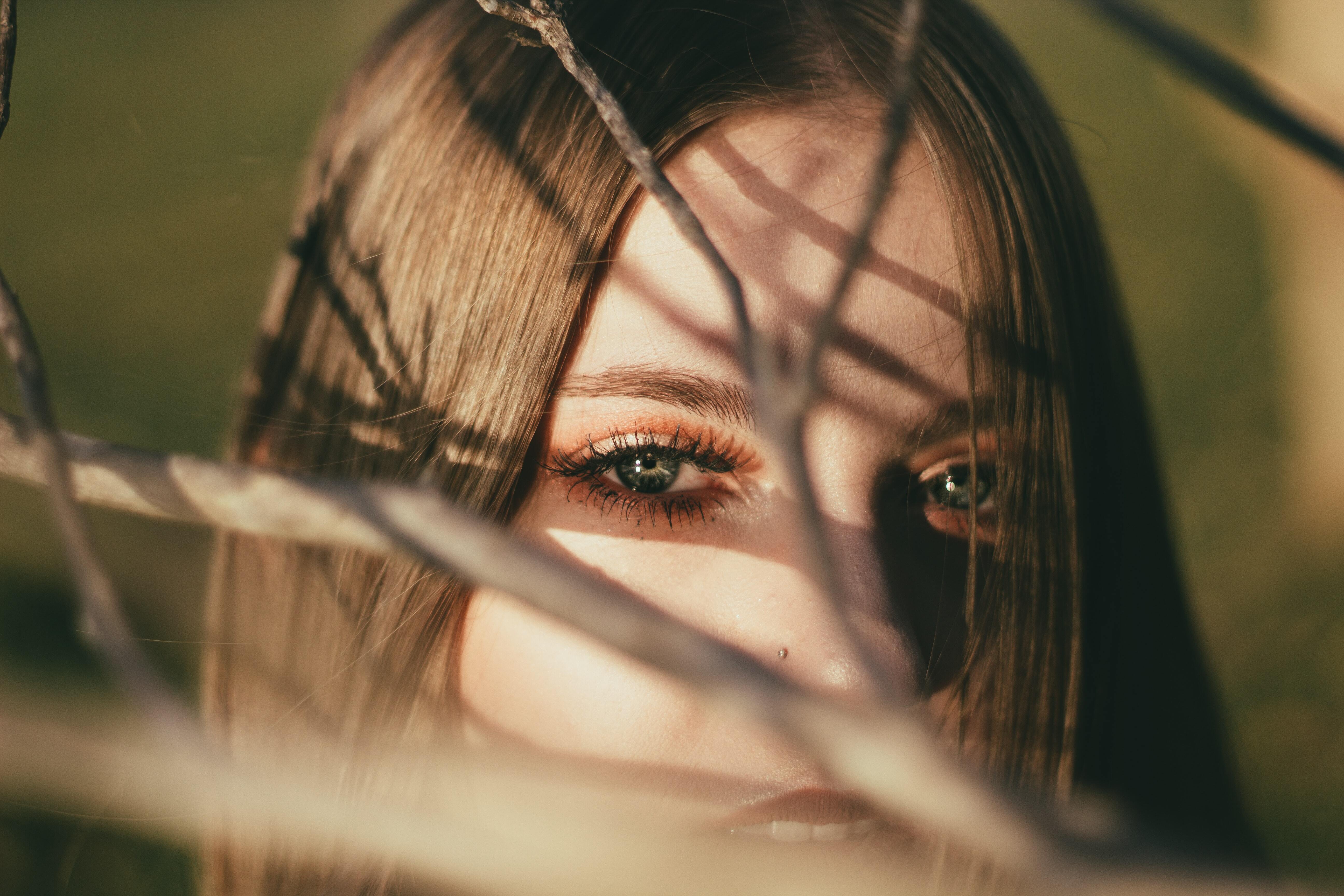 A woman wearing makeup stands behind branches